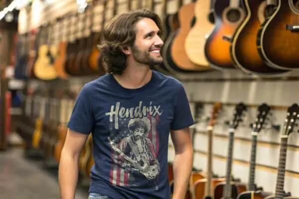 A smiling man browsing guitars in a musical instrument shop, featuring a variety of acoustic guitars hanging on display.