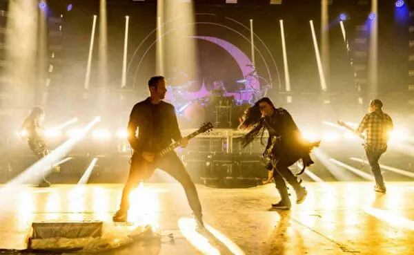 Guitarists and vocalist performing energetically on stage during a SocieTees concert with vibrant lighting effects.