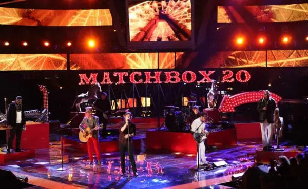 Bright stage with Matchbox 20 sign, band playing guitars, drums, and vocals during concert. Colorful lighting creates energetic atmosphere.