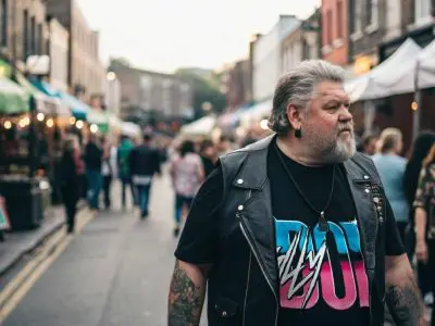 A stylish man with tattoos exploring a vibrant outdoor market on a lively street.