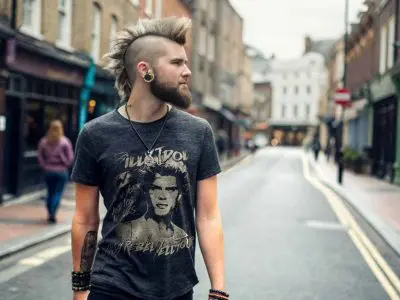 A trendy punk rock man with a mohawk hairstyle, tattoos, and eclectic accessories walking through an urban street.