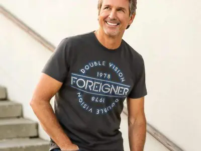Happy middle-aged man wearing a T-shirt with "Foreigners" printed on it, smiling while walking up stairs. Fashionable casual wear for men, leisure style, trending T-shirt design.