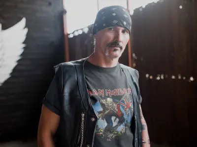 A stylish man wearing a bandana and Iron Maiden t-shirt, showcasing a cool rocker vibe with a leather vest and tattoos.