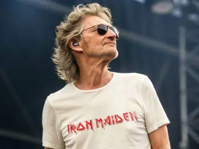 Aging rock singer wearing sunglasses and Iron Maiden t-shirt performing on stage at a concert, showcasing passion for music and classic rock style.