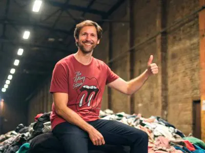 Alt: Man smiling and giving a thumbs-up while sitting on a mountain of clothing in an industrial space.