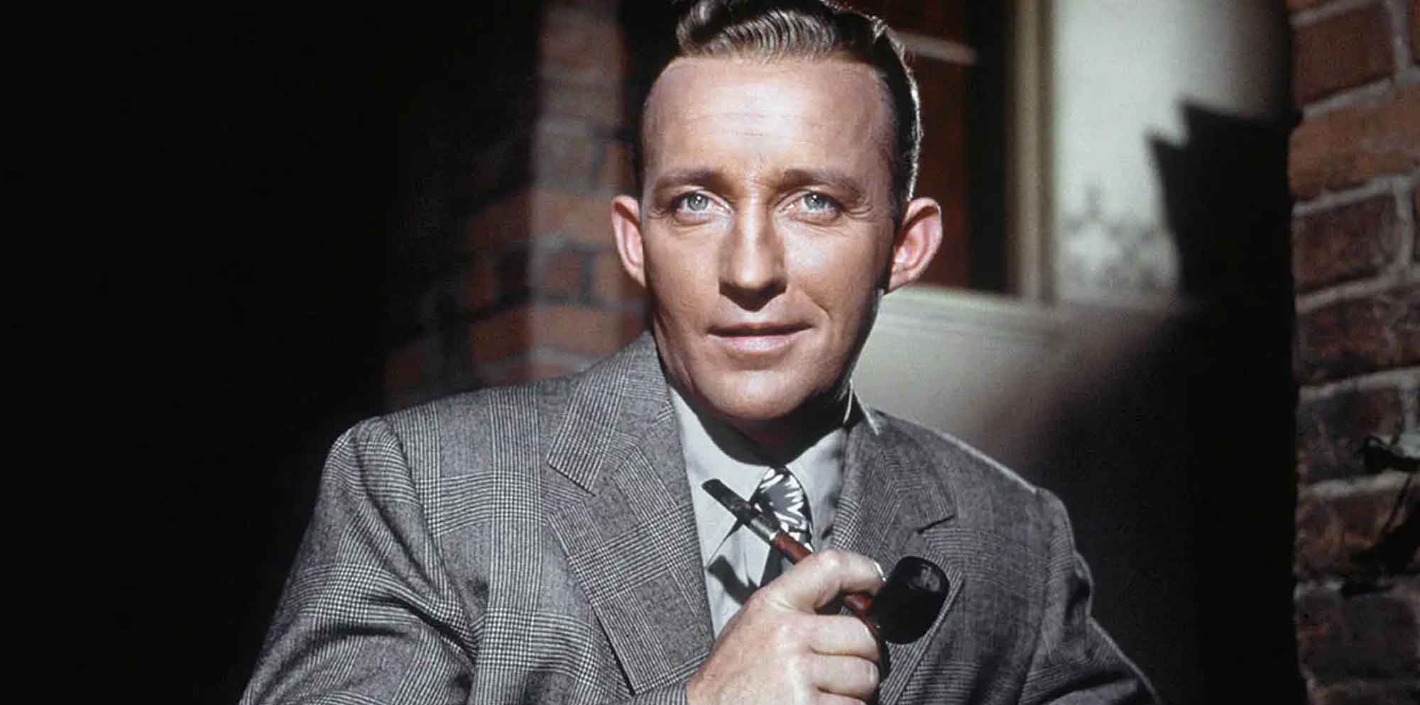 Vintage film scene featuring a man in a suit holding a cigarette against a brick wall background.