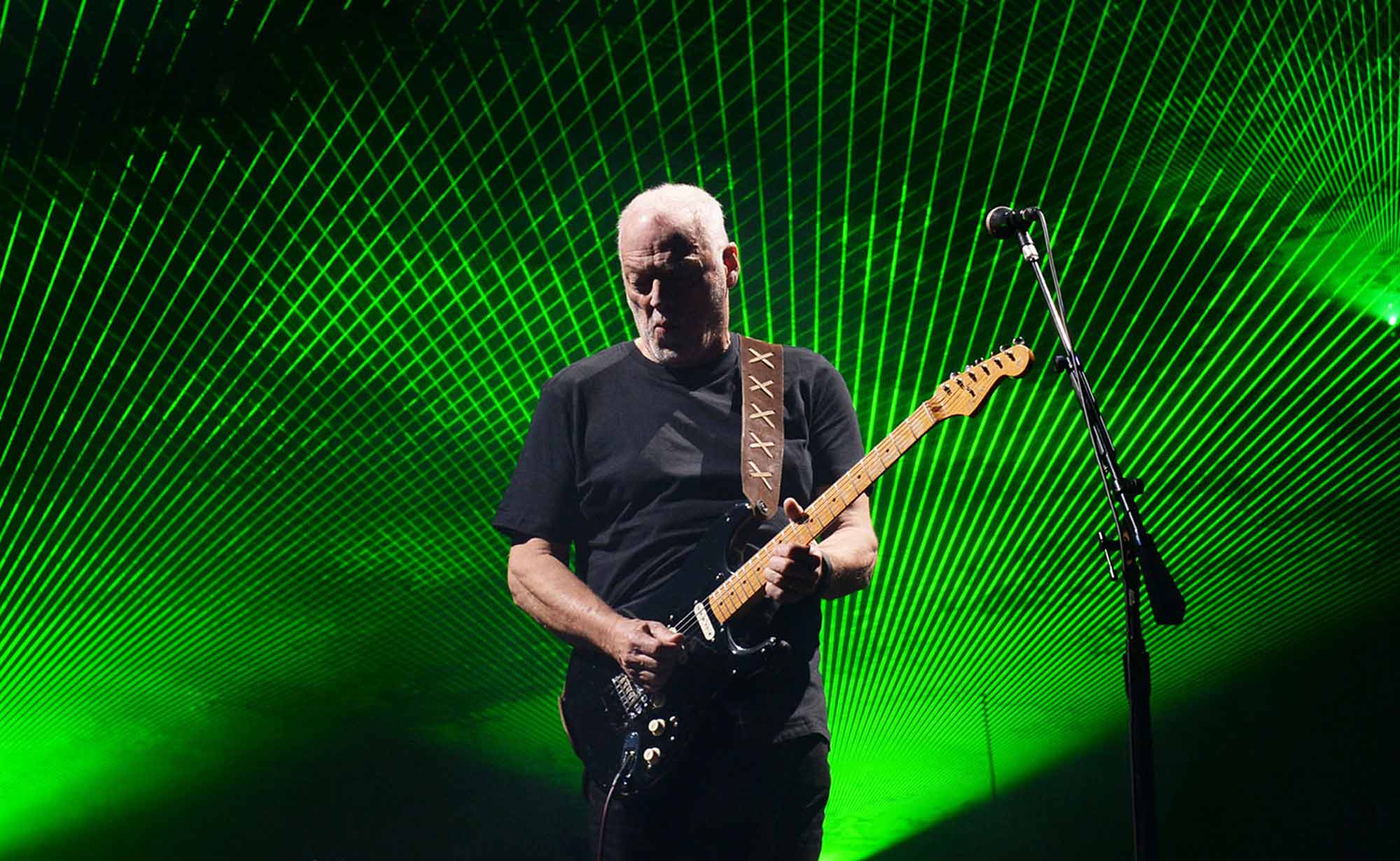 A guitarist playing passionately on stage with green laser light effects creating an electrifying concert atmosphere.