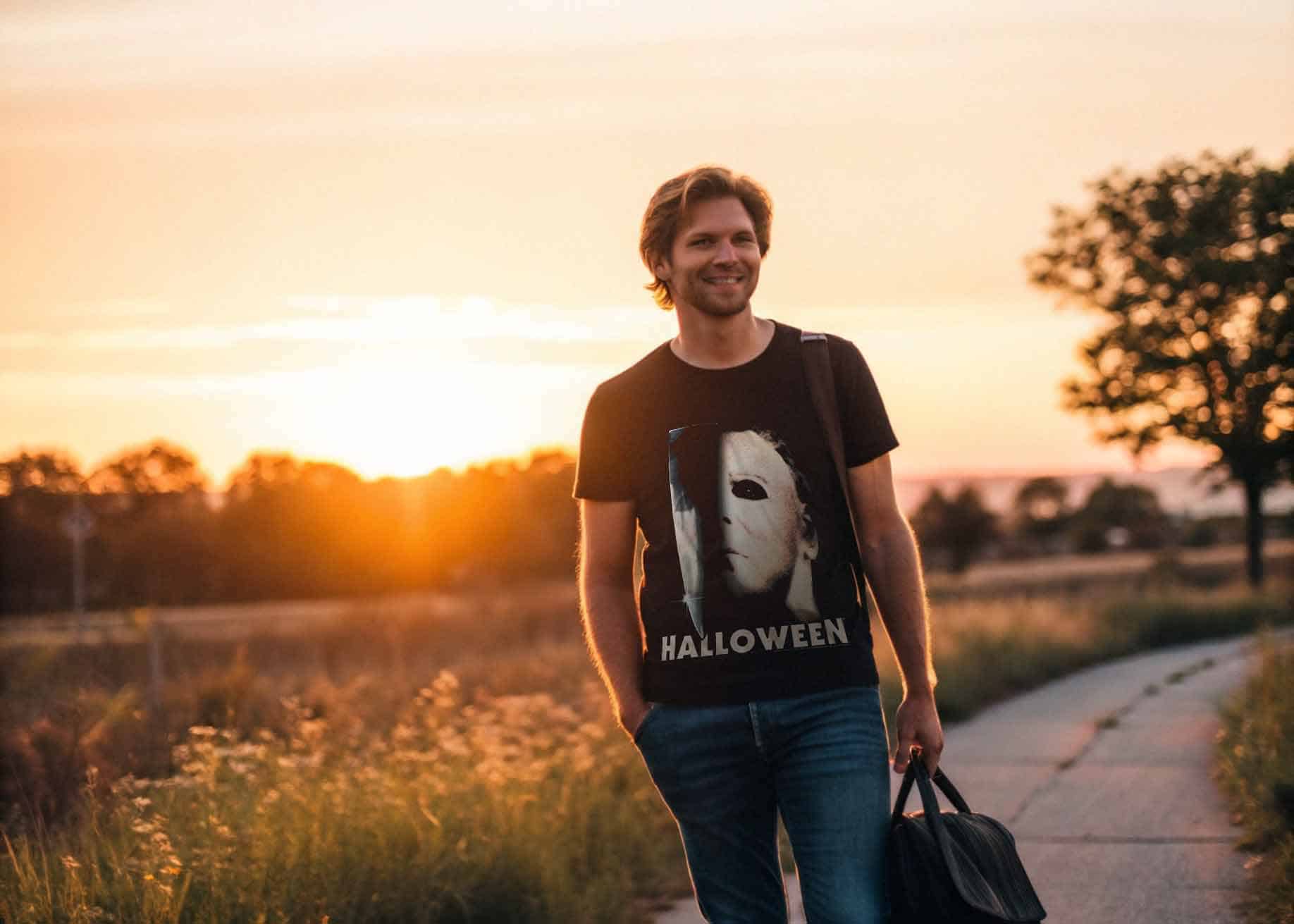 Man smiling in casual wear with Halloween graphic on T-shirt during sunset.