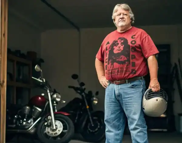 Handsome middle-aged man with helmet, standing next to vintage motorcycle in garage.