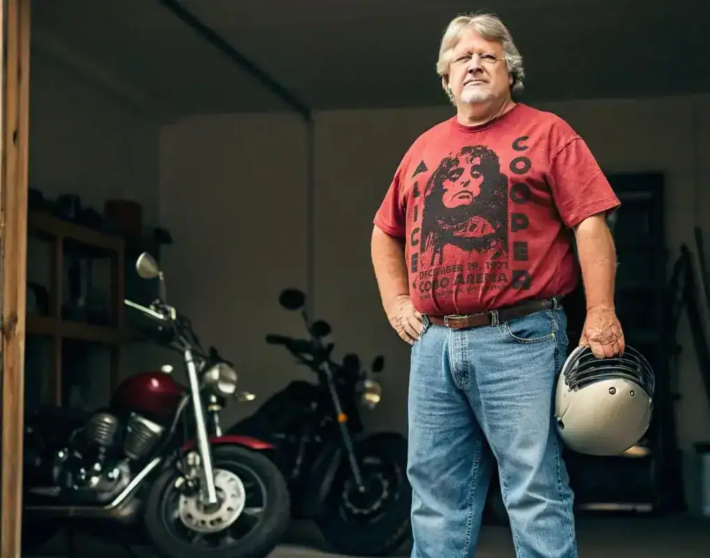 Handsome middle-aged man with helmet, standing next to vintage motorcycle in garage.