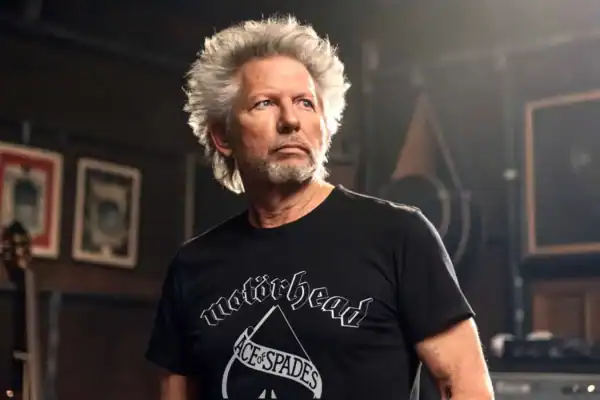 A stylish older man with white hair wearing a Motörhead T-shirt in a creative studio or music space.