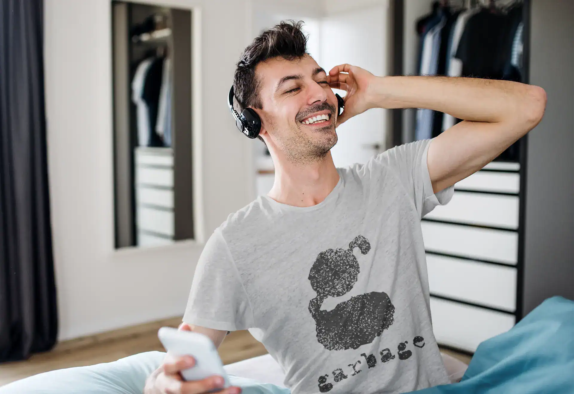 Happy man listening to music with wireless headphones, relaxing at home, wearing a graphic t-shirt.