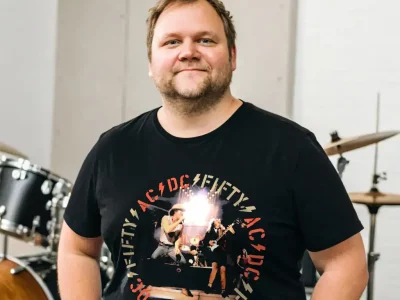 Man in black AC/DC band tee with musical band on stage design, music, performance.