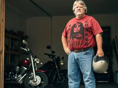 Handsome middle-aged man with helmet, standing next to vintage motorcycle in garage.