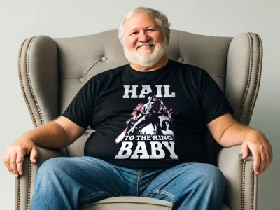 Alt text: Man wearing a black "Hail to the King Baby" T-shirt, sitting in a gray armchair.
