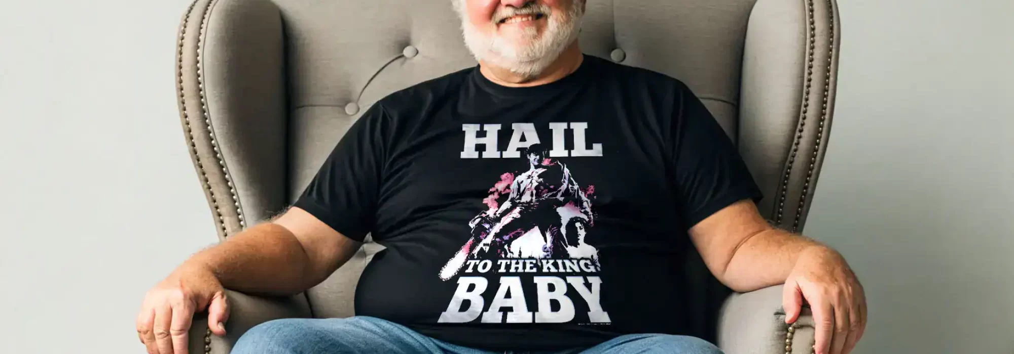 Alt text: Man wearing a black "Hail to the King Baby" T-shirt, sitting in a gray armchair.