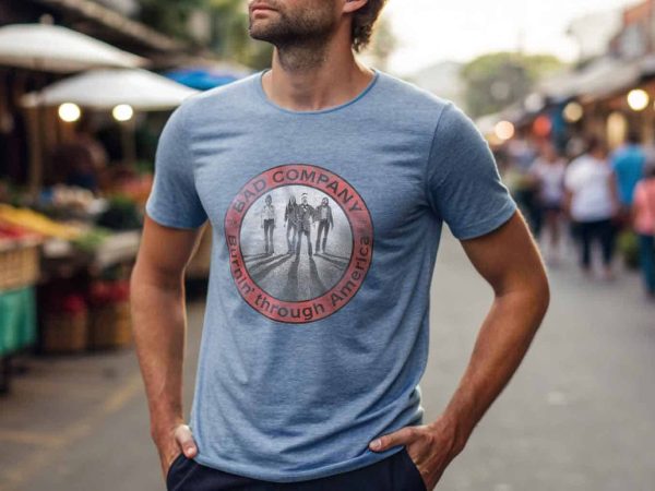 A man wearing a stylish graphic T-shirt with "Bad Company" printed on it, shopping at an outdoor market street scene.