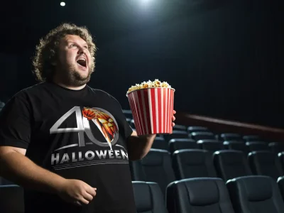 Person holding a large striped popcorn bucket in a dark movie theater.