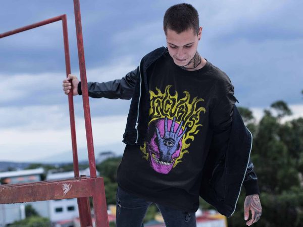 A young man with tattoos wearing a graphic T-shirt and jacket, standing outdoors against a cloudy sky, showcasing urban streetwear fashion.