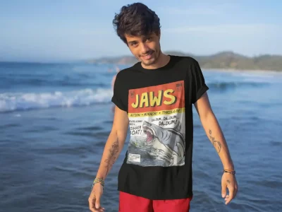 Boy wearing Jaws graphic tee on a beach with ocean waves in background.