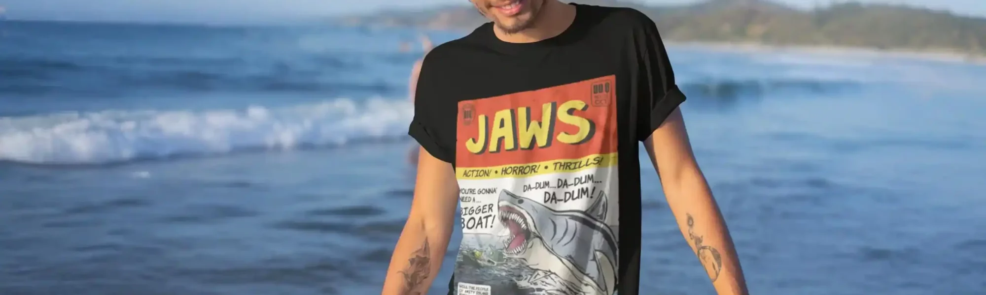 Boy wearing Jaws graphic tee on a beach with ocean waves in background.