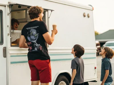 Young man with ice cream talking to two boys near ice cream truck.