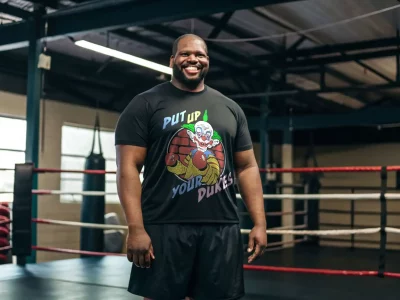 Happy man in boxing gym wearing a black t-shirt with colorful clown graphic and boxing gloves illustration.