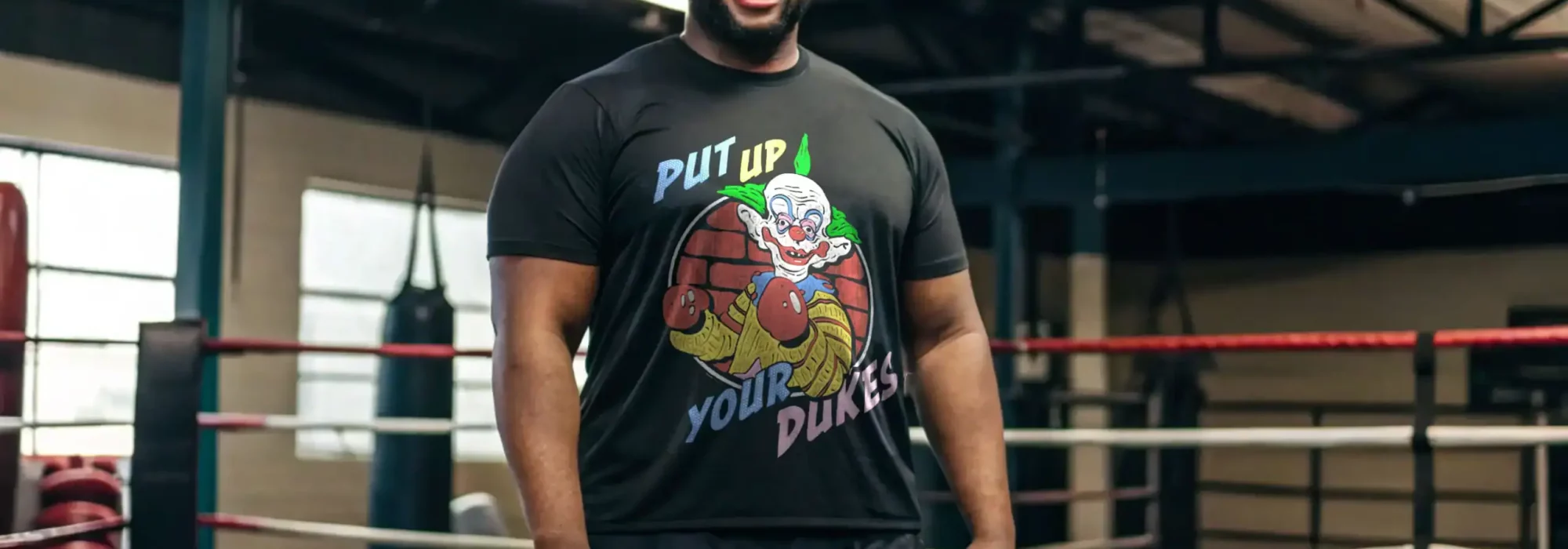 Happy man in boxing gym wearing a black t-shirt with colorful clown graphic and boxing gloves illustration.
