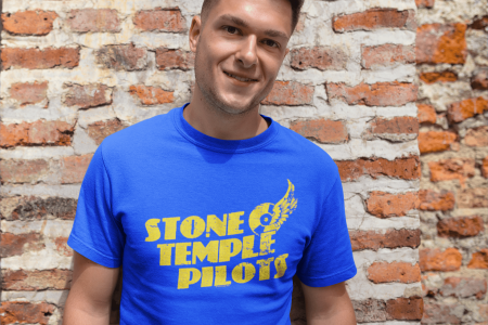 Youthful male smiling in Stone Temple Pilots T-shirt against rustic brick wall, casual fashion, rock band fan, street style.