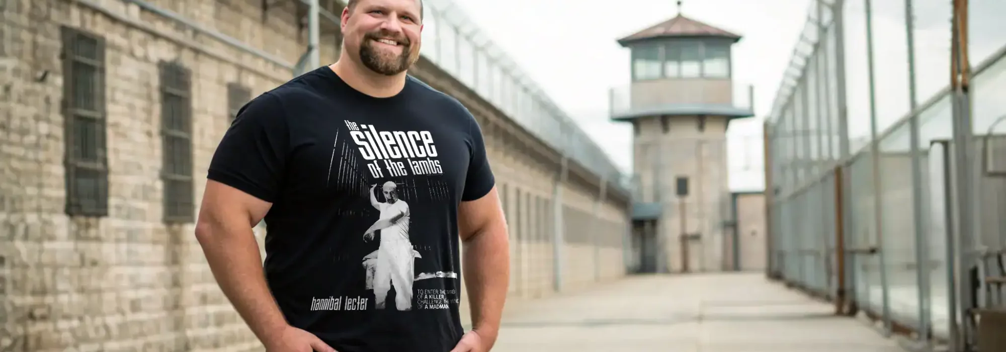 An individual wearing a black graphic T-shirt inspired by the movie "The Silence of the Lambs" at a historic prison site.