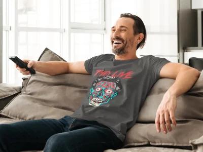 Smiling man in casual clothes relaxing on sofa, holding remote, enjoying leisure time at home.
