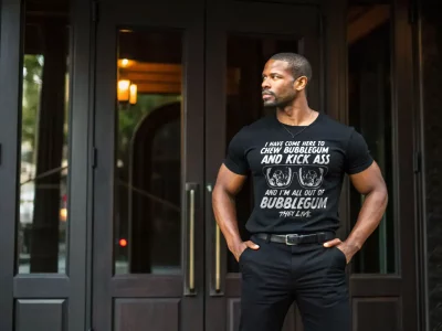 Man in black graphic t-shirt with humorous quote standing outside modern building.