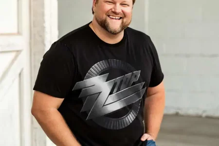 Man in black SocieTees graphic T-shirt, casual pose, smiling and happy.