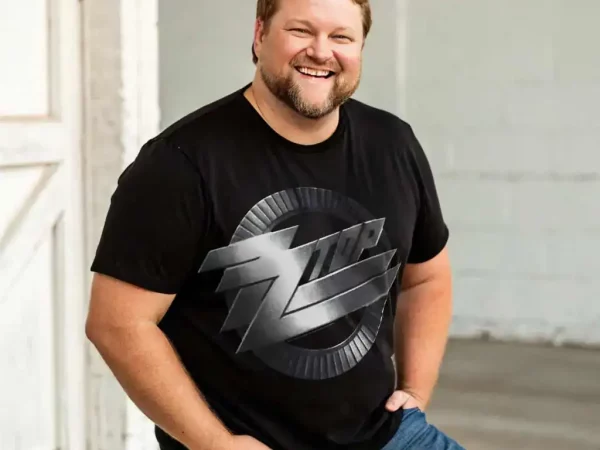 Man in black SocieTees graphic T-shirt, casual pose, smiling and happy.