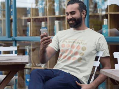 Relaxed man enjoying a moment outdoors with his smartphone, wearing a vintage-inspired graphic t-shirt, surrounded by modern decor and vibrant colors.