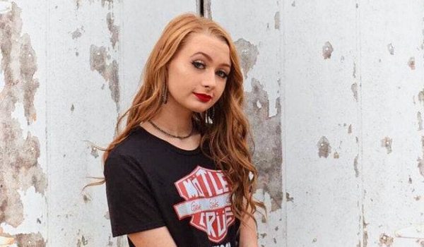Casual young woman wearing a Harley Davidson t-shirt, sitting outdoors against a weathered wall, showcasing trendy streetwear fashion.