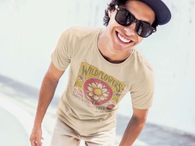 Cheerful man wearing sunglasses and a beige graphic T-shirt with floral design, enjoying a sunny day outdoors, promoting casual streetwear, happiness, and summer fashion.