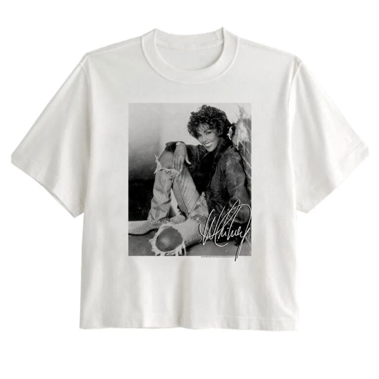Black-and-white vintage-style t-shirt with a woman smiling and sitting in a casual pose, featuring an artistic signature.