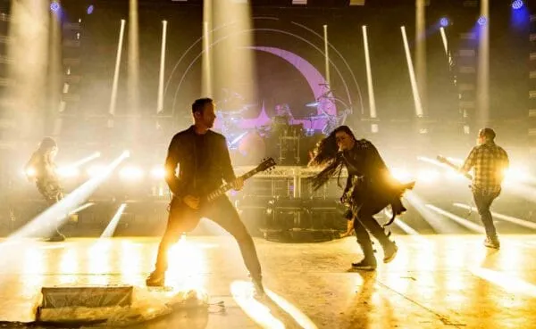 Guitarists and vocalist performing energetically on stage during a SocieTees concert with vibrant lighting effects.