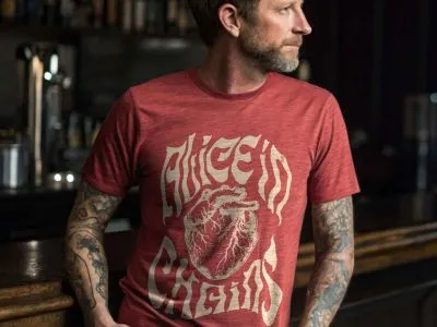 Stylish man in a graphic tee with medical-themed artwork, tattoos, and a contemplative look in a cozy bar.
