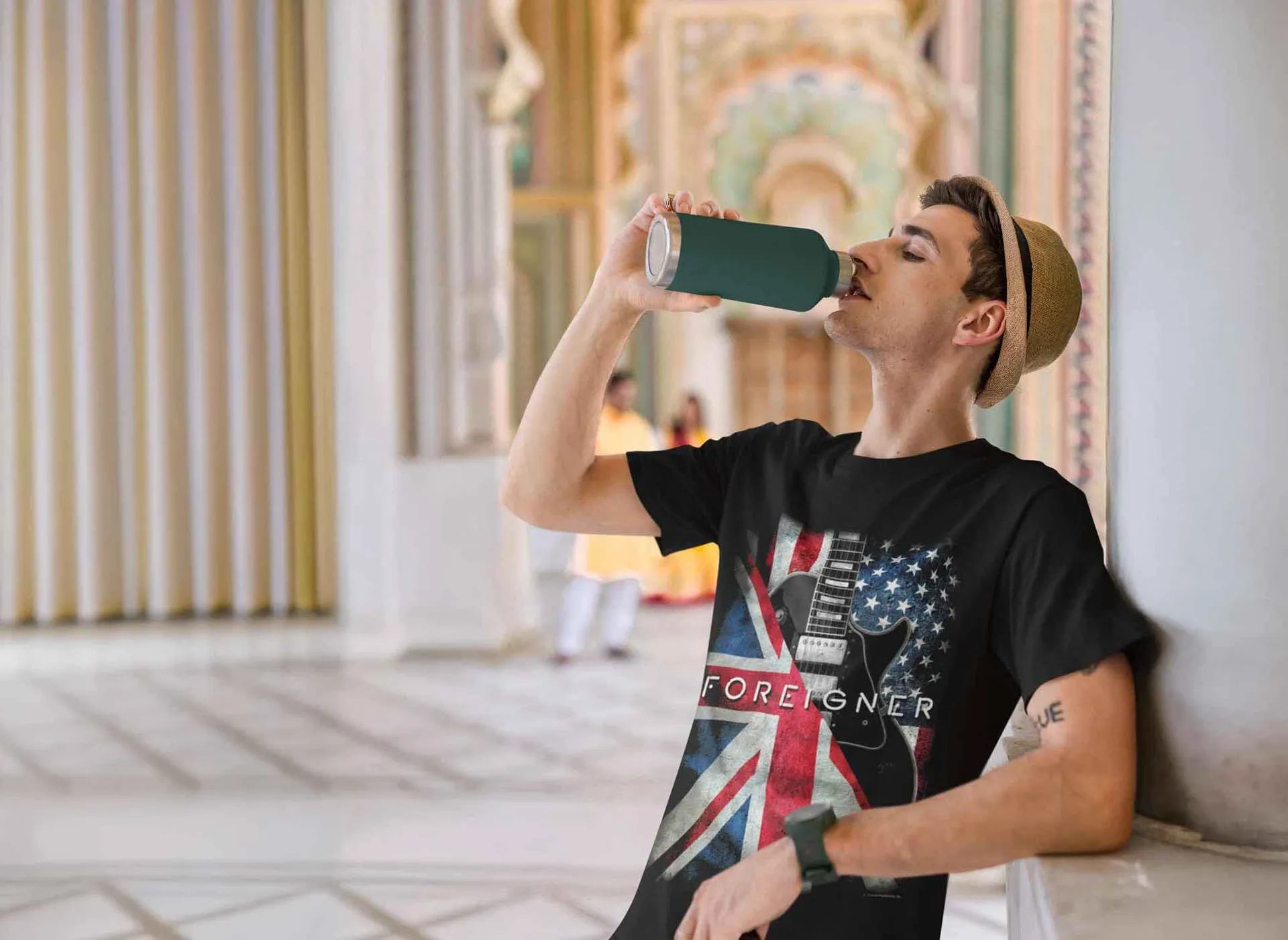 Young man drinking from a reusable tumbler at a cultural or historical site.