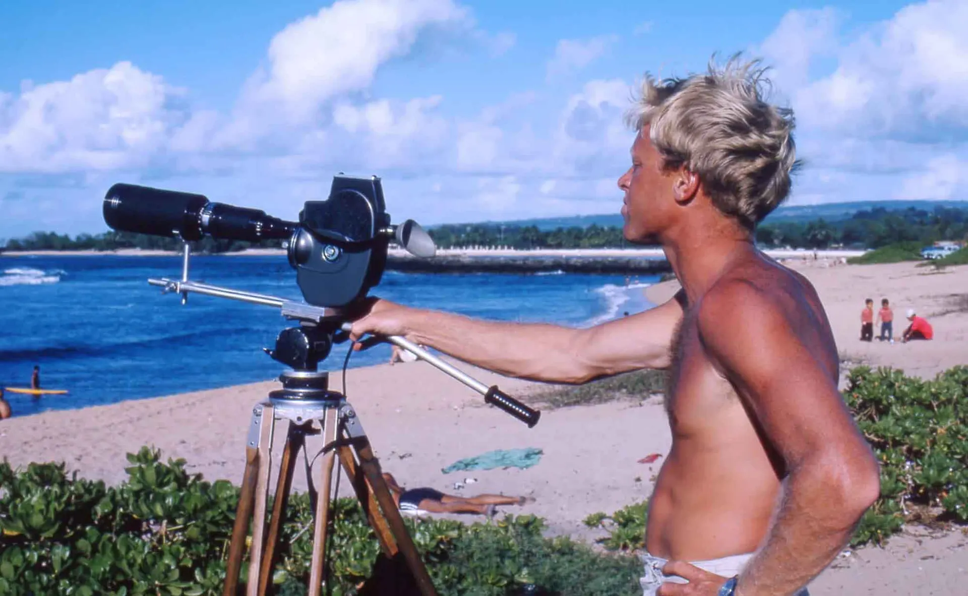 Outdoor beach scene with man looking through telescope by the ocean, sunny weather and people enjoying the day.
