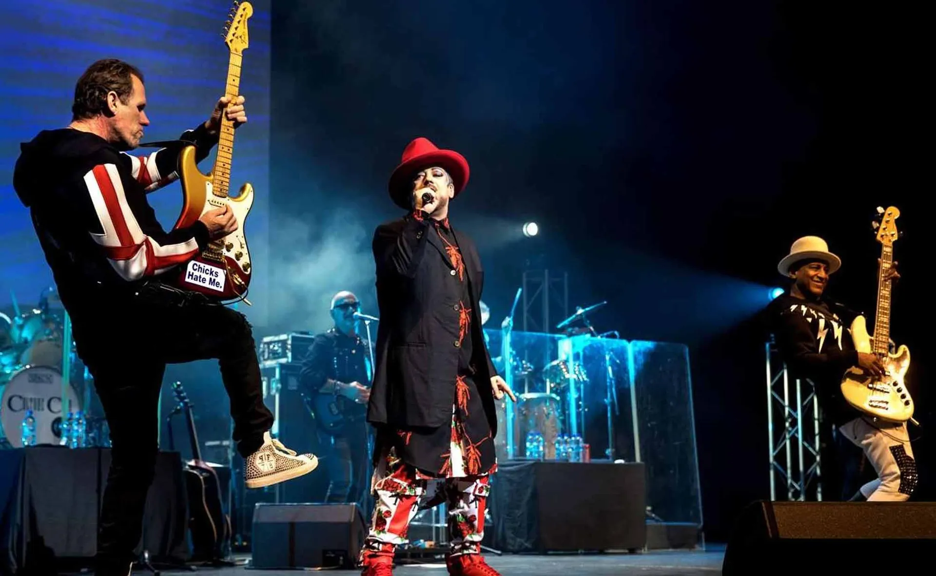 Artist performing on stage with guitar and microphones during a live concert event, emphasizing musical entertainment.