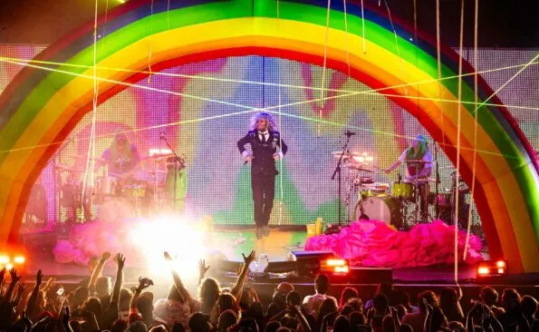 Colorful rainbow stage with live band and enthusiastic crowd at a music festival.