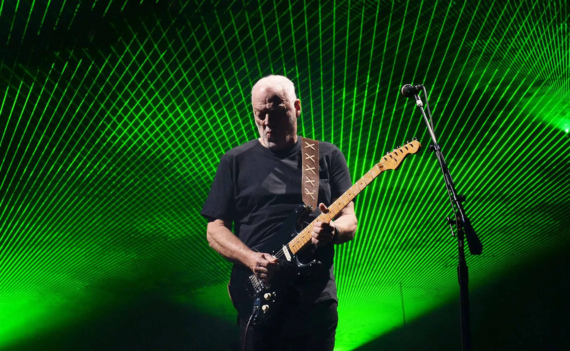 A guitarist playing passionately on stage with green laser light effects creating an electrifying concert atmosphere.