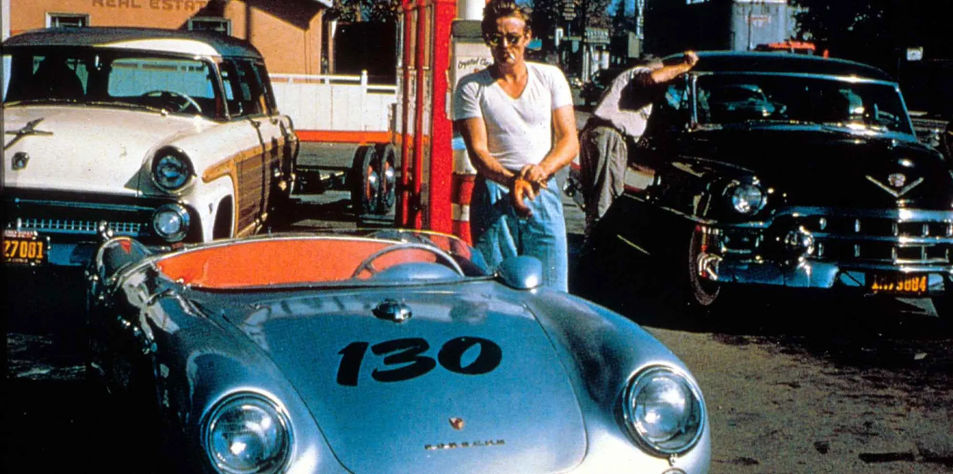 Retro sports car parked among classic cars and street scene in urban setting.