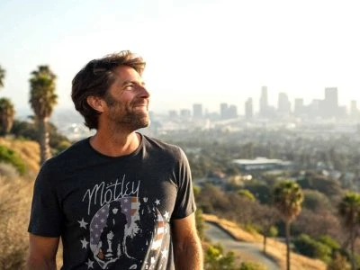 A man delightedly gazes at the Los Angeles skyline during sunset, wearing a black Mötley Crüe t-shirt, capturing city and nature.