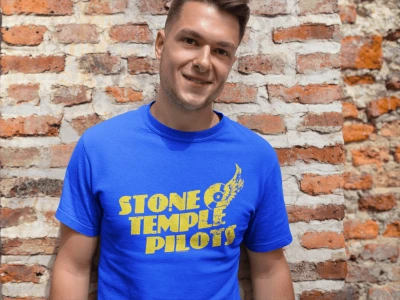 Youthful male smiling in Stone Temple Pilots T-shirt against rustic brick wall, casual fashion, rock band fan, street style.
