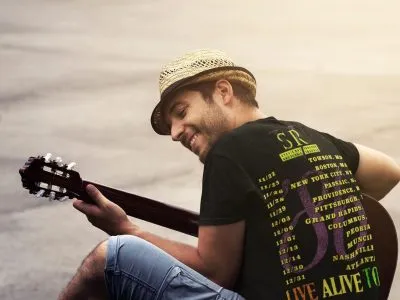 A young man wearing a straw hat plays an acoustic guitar outdoors during sunset, smiling, creating a relaxed, musical vibe perfect for street performance or leisure.