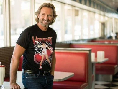 Relaxed man wearing graphic T-shirt in classic American diner setting, showcasing vintage ambiance and retro style.